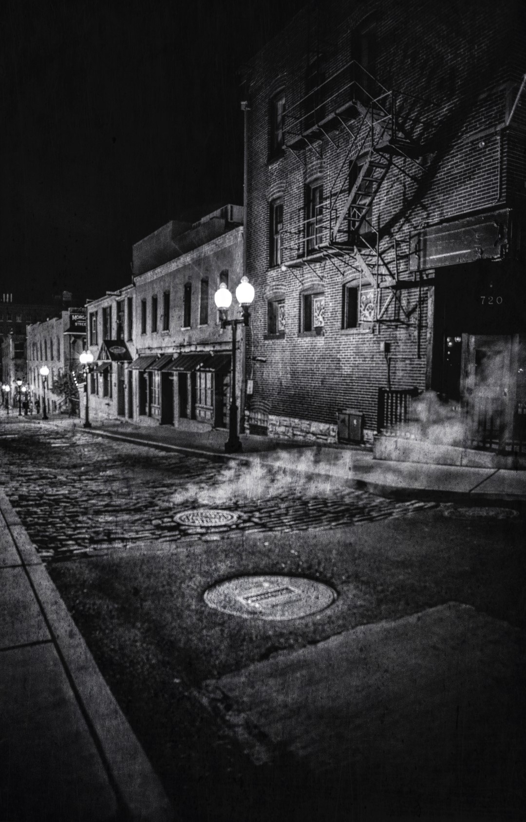 Steam escapes from a manhole along a street in Laclede's Landing at night.